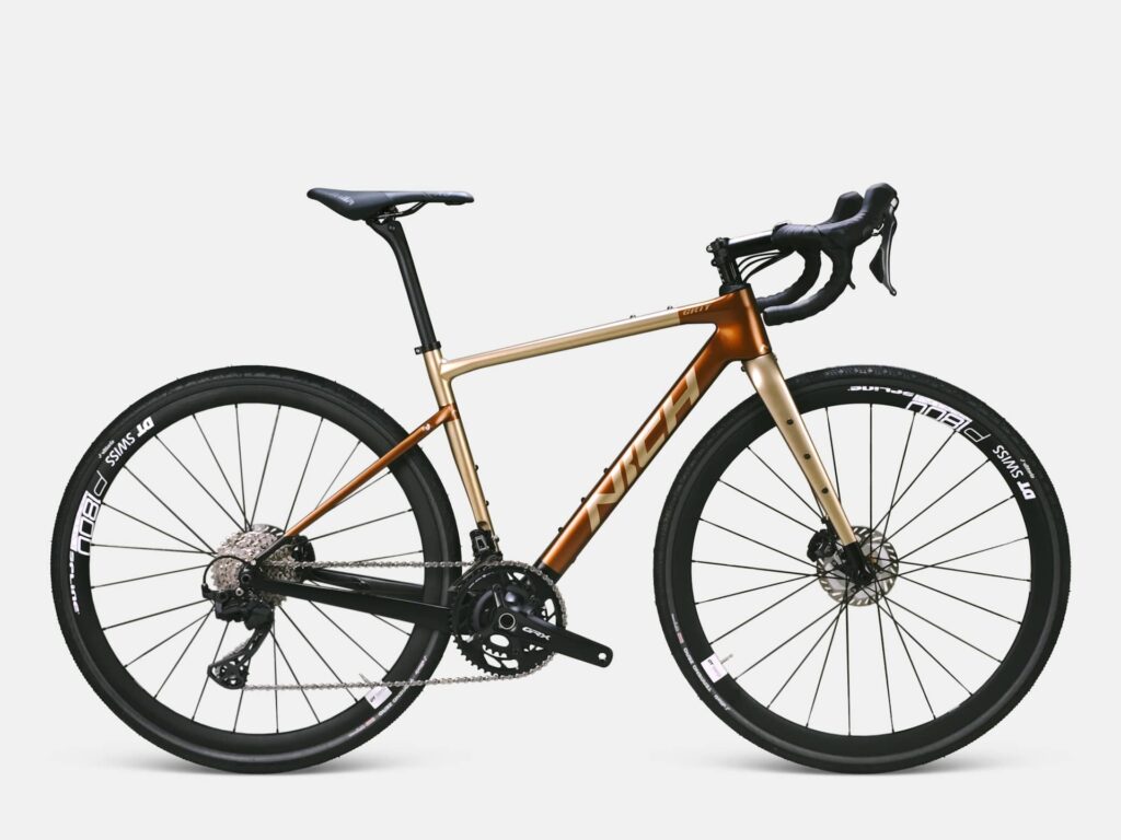 Studio photo of the bronze Nich Grit carbon gravel bike with 40mm tires, built to handle off-the-beaten-path trails on our gravel tours.