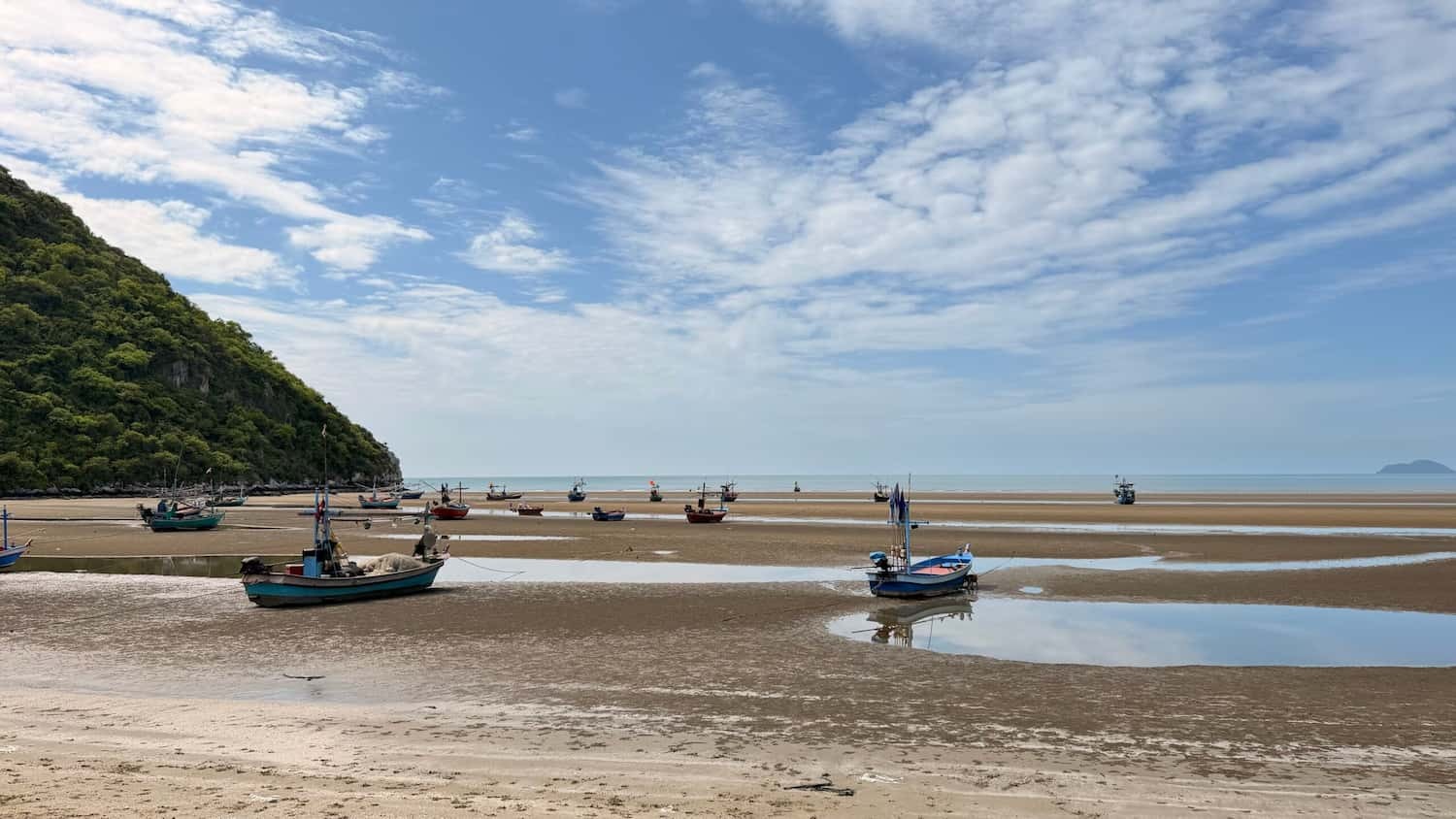 Traditional Thai fishing boats resting on the wet sand of Khao Kalok beach during low tide in Pranburi, a scenic stop on our bicycle tours.