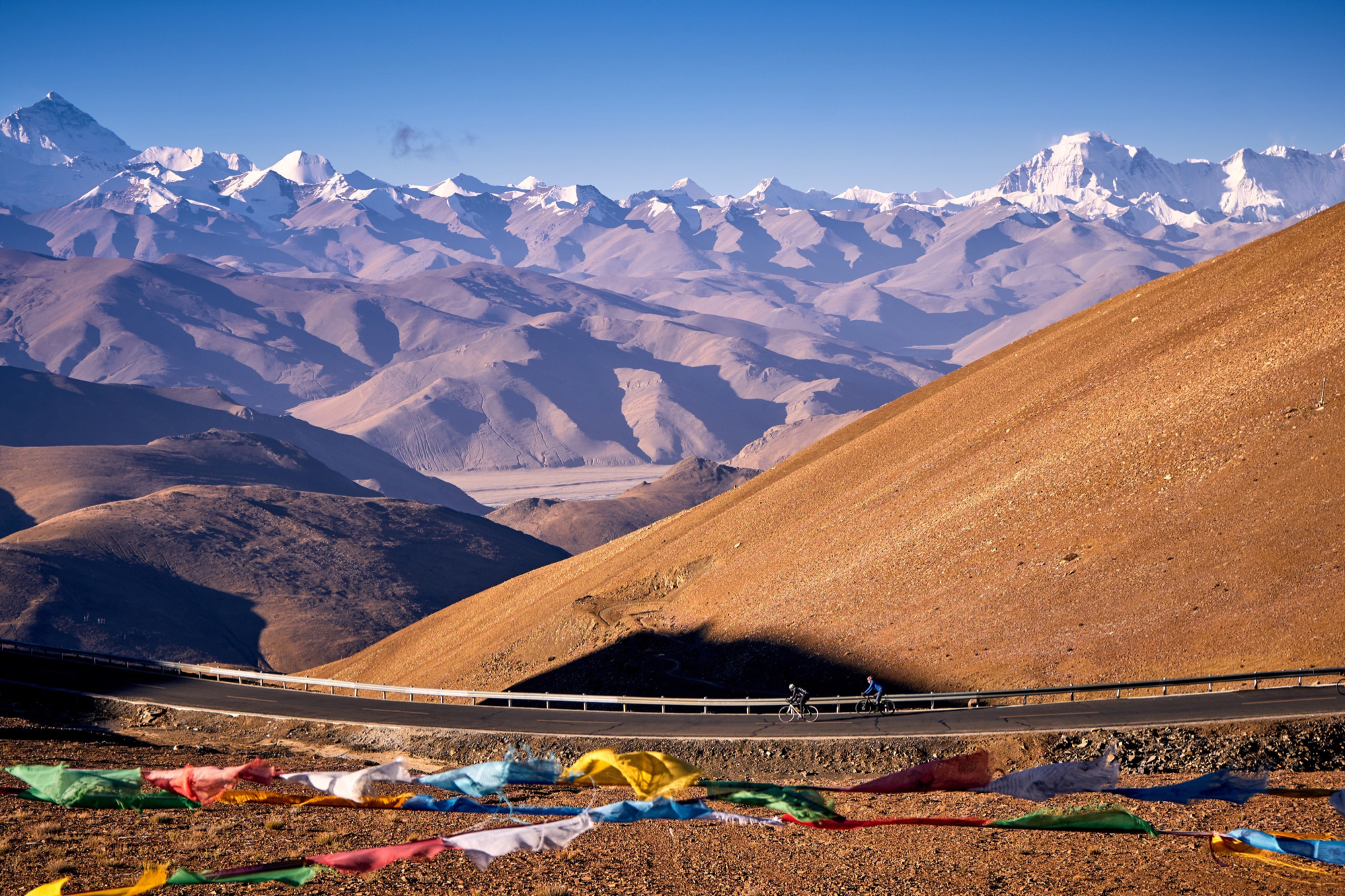 Winding paved roads leading toward snow-capped Himalayan peaks on the Epic Tibet road cycling expedition.