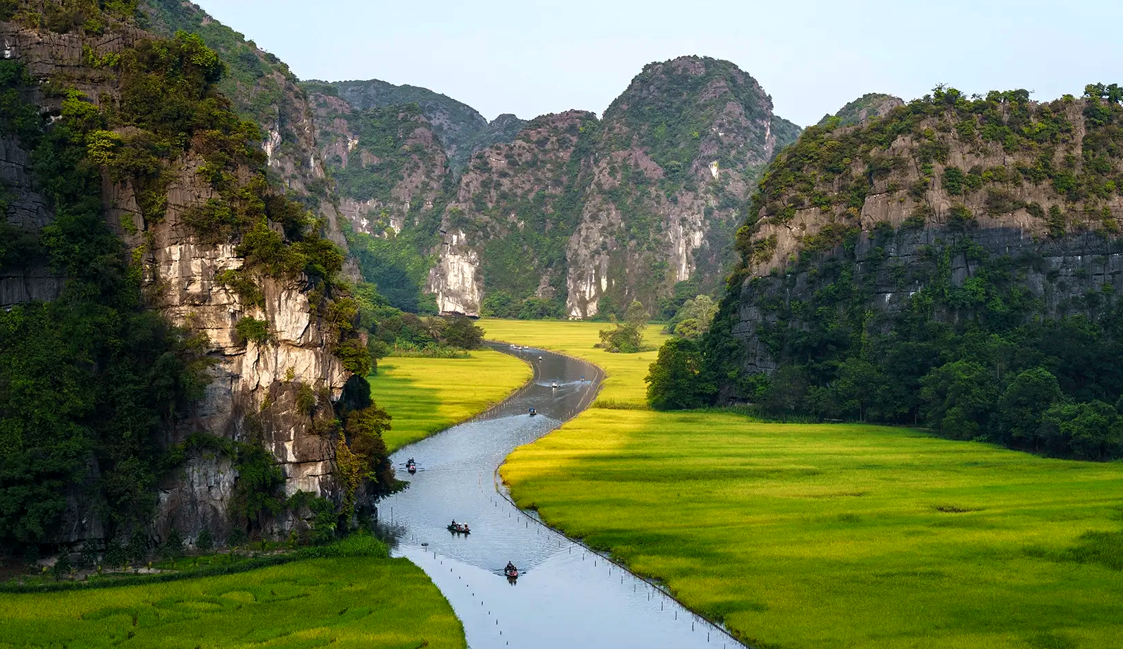 The stunning landscape of Tam Coc in Ninh Binh, featuring a river winding through green rice fields between limestone peaks during our Bangkok to Hanoi tour.
