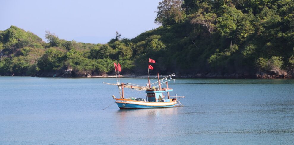 A traditional wooden fishing boat floating on calm turquoise waters near a forested island shoreline on our coastal cycling tours.