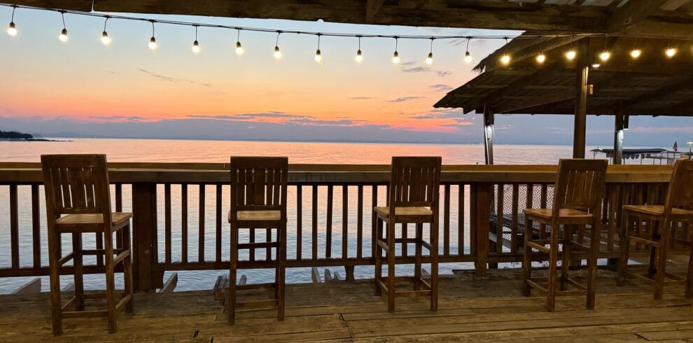 A stunning orange sunset over the sea, viewed from a rustic wooden bar deck on a relaxing rest day.
