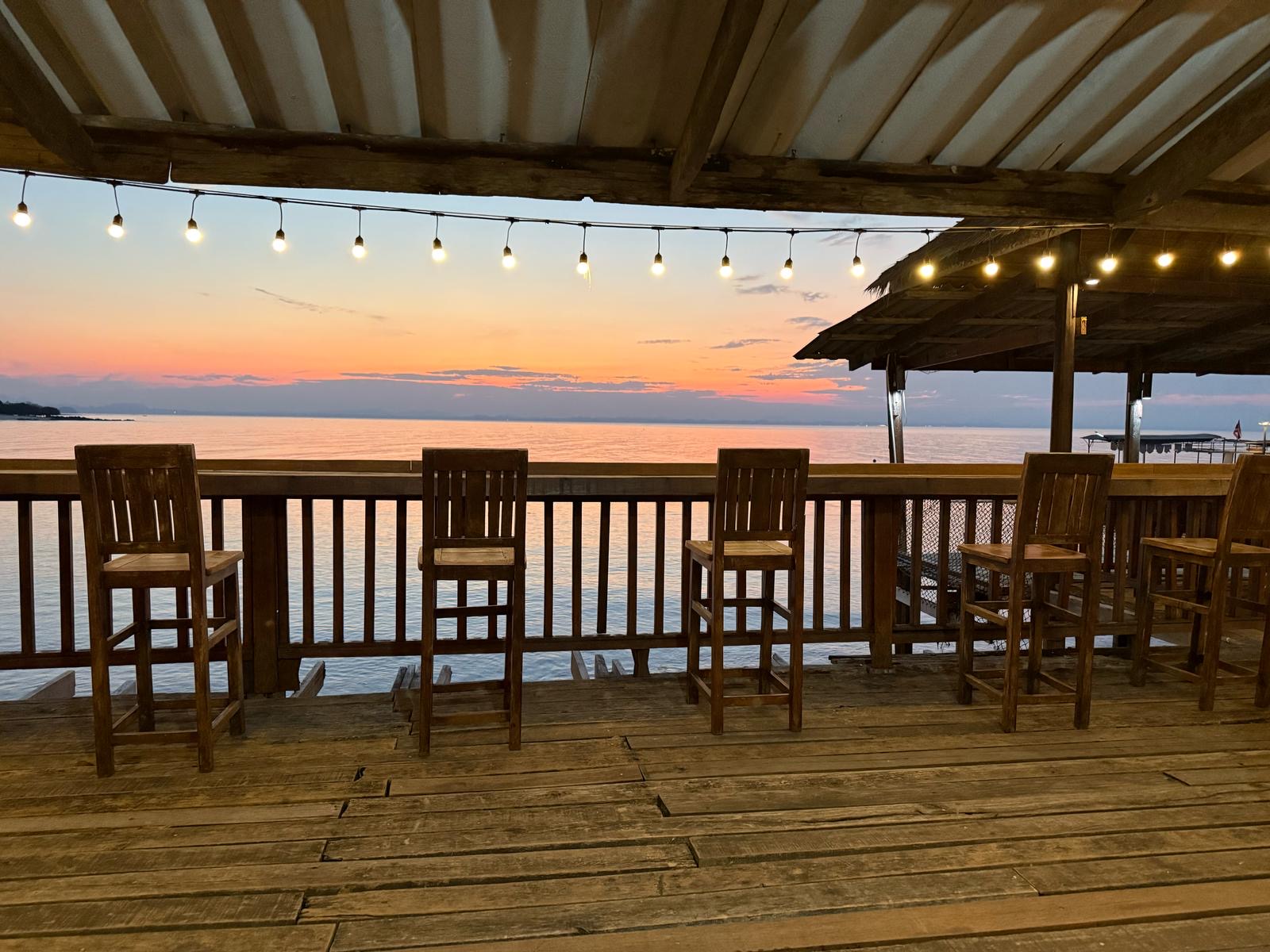 A stunning orange sunset over the sea, viewed from a rustic wooden bar deck on a relaxing rest day.