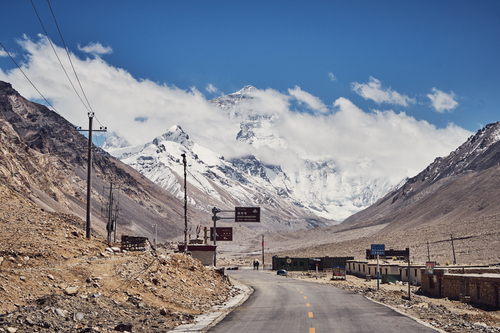 A road cyclist's view of the paved route towards Mount Everest under a cloudy sky during the Epic Tibet road cycling expedition.