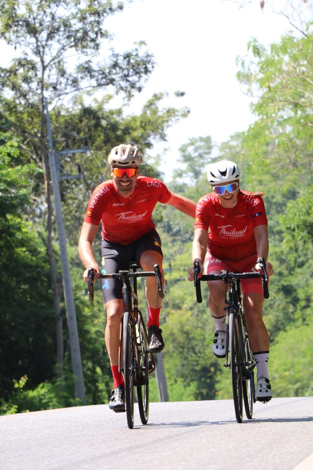 Two road cyclists in matching red jerseys riding side-by-side up a hill climb on a fully supported cycling holiday in Thailand.