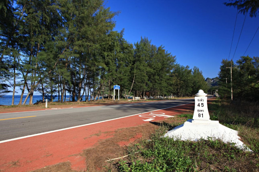 A smooth, dedicated red cycle path along a scenic coastal road in Southern Thailand, offering ideal conditions for a road bike tour.