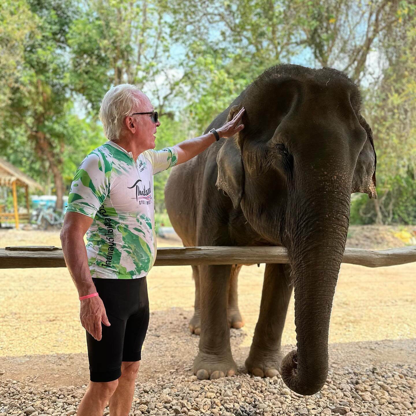 A senior road cyclist wearing a green and white team kit interacting with an elephant during an elephant safari excursion.