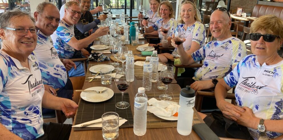 Group of international cyclists from Thailand Cycle Tours enjoying a post-ride lunch at a restaurant in Thailand, raising glasses in celebration. The image captures the social side of a guided cycling holiday, featuring local cuisine, camaraderie, and memorable travel experiences in a relaxed dining setting.
