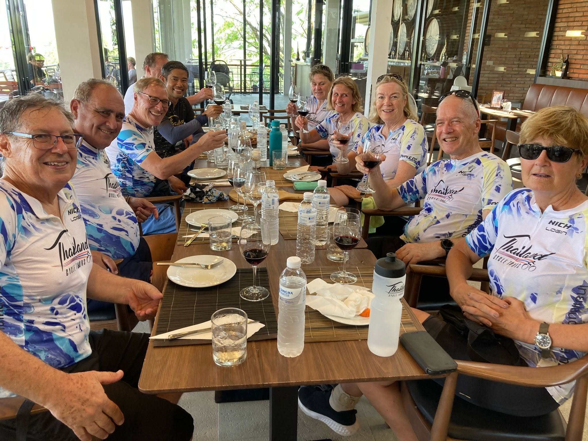 Group of international cyclists from Thailand Cycle Tours enjoying a post-ride lunch at a restaurant in Thailand, raising glasses in celebration. The image captures the social side of a guided cycling holiday, featuring local cuisine, camaraderie, and memorable travel experiences in a relaxed dining setting.