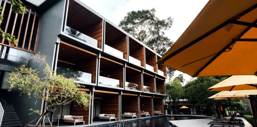 Modern boutique resort with spacious balconies overlooking a tranquil swimming pool, surrounded by tropical gardens and contemporary architecture in Thailand.