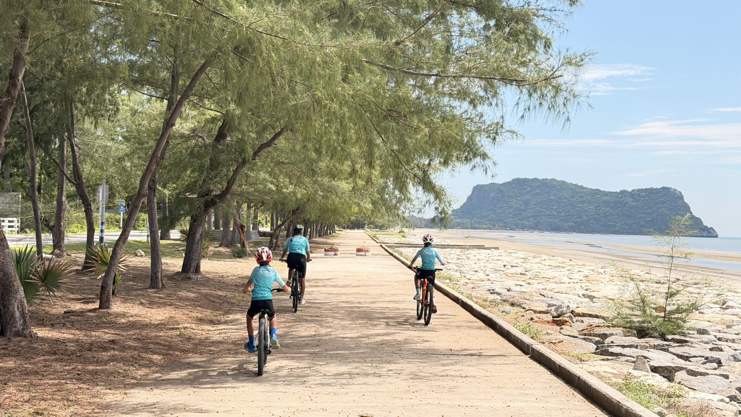Kids cycling along a scenic beach road in Thailand with ocean views, palm trees, and a safe family-friendly cycling route during a Thailand Cycle Tours adventure.