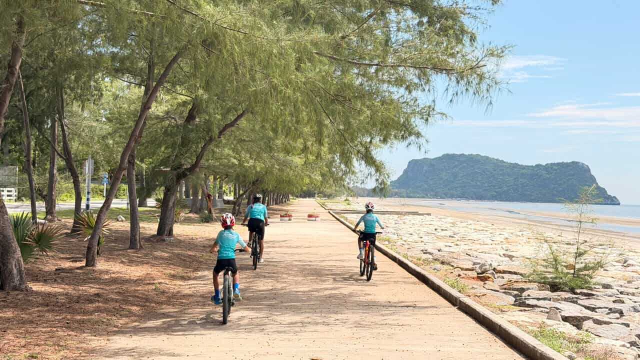 Kids cycling along a scenic beach road in Thailand with ocean views, palm trees, and a safe family-friendly cycling route during a Thailand Cycle Tours adventure.
