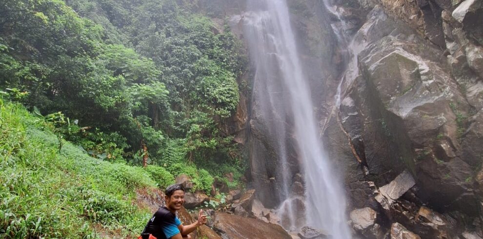 Hiker beside a tall waterfall in a lush tropical rainforest.