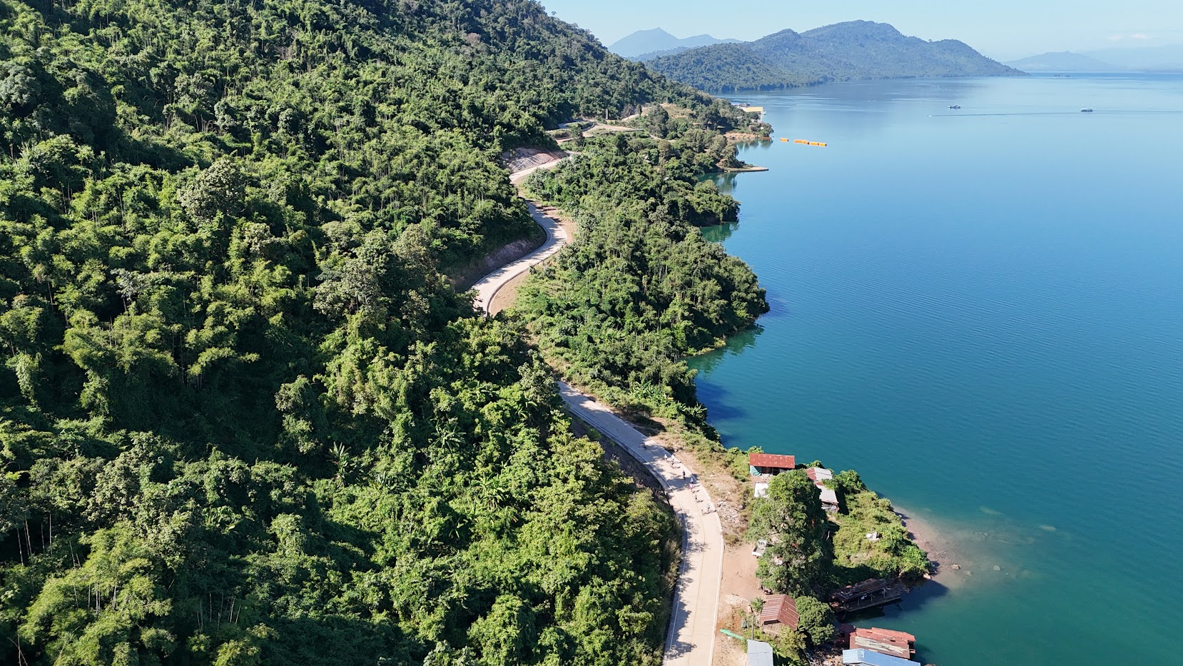Cyclists riding on a beautiful scenic road along Nam Ngum Lake in Laos, surrounded by tranquil blue water, rolling hills, and lush tropical landscapes during a cycling tour with Thailand Cycle Tours.