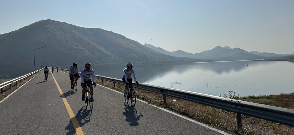 Cyclists riding beside a scenic lake and mountains on a Thailand cycling tour