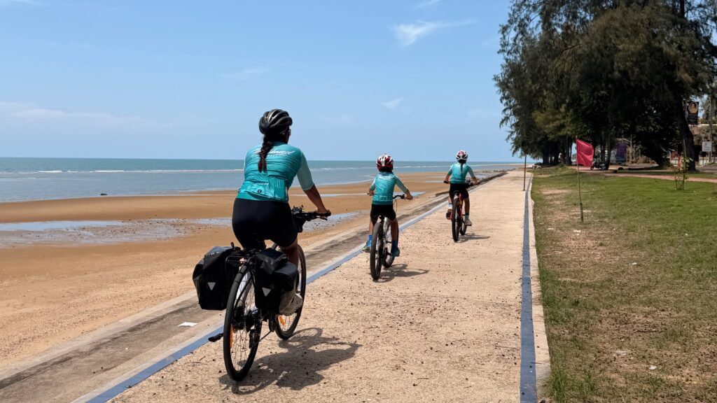 Radfahrer fahren entlang eines malerischen Strandes auf einer Küsten-Radtour in Thailand.