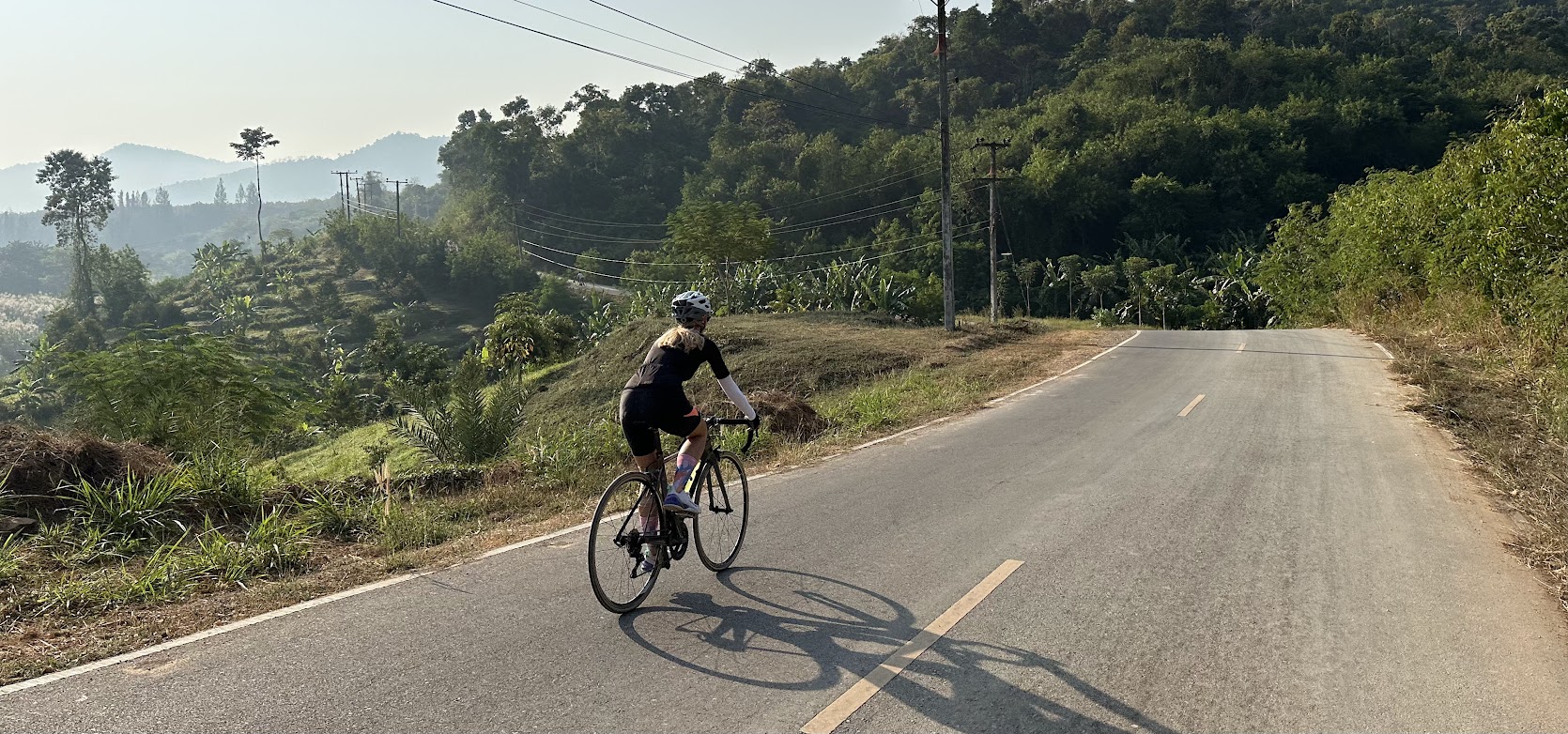 Rennradfahrer auf einer malerischen Strecke durch die ruhige, hügelige Landschaft nahe Hua Hin, Thailand.